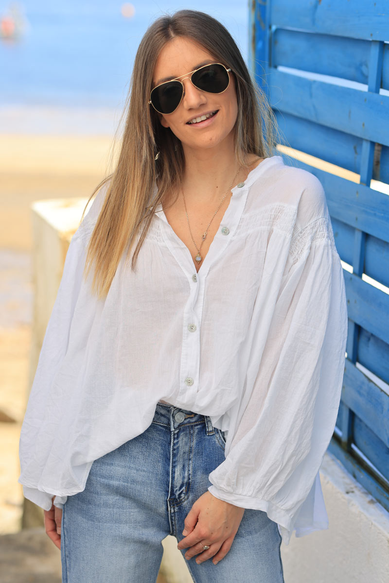 Blusa blanca de algodón con mangas anchas, botones nacarados y cuello fruncido.