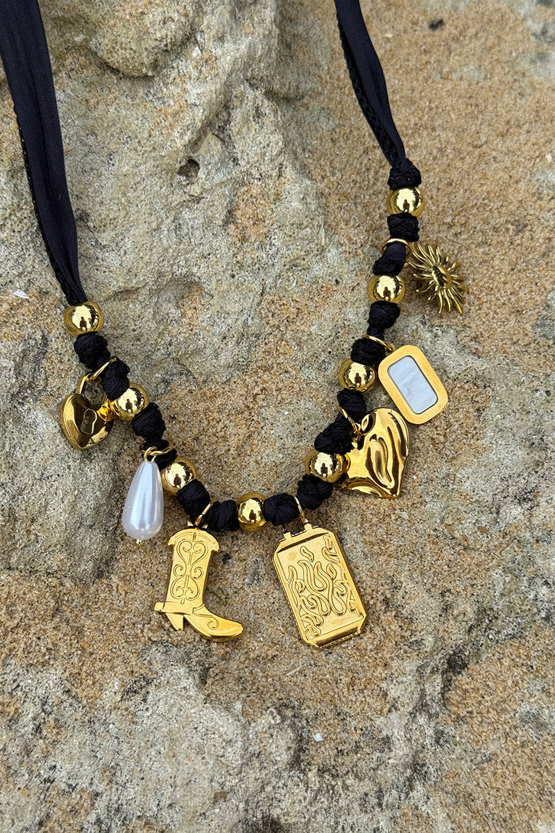 Collar de cinta negra y colgantes dorados, bota vaquera, corazón de sol de Santiago