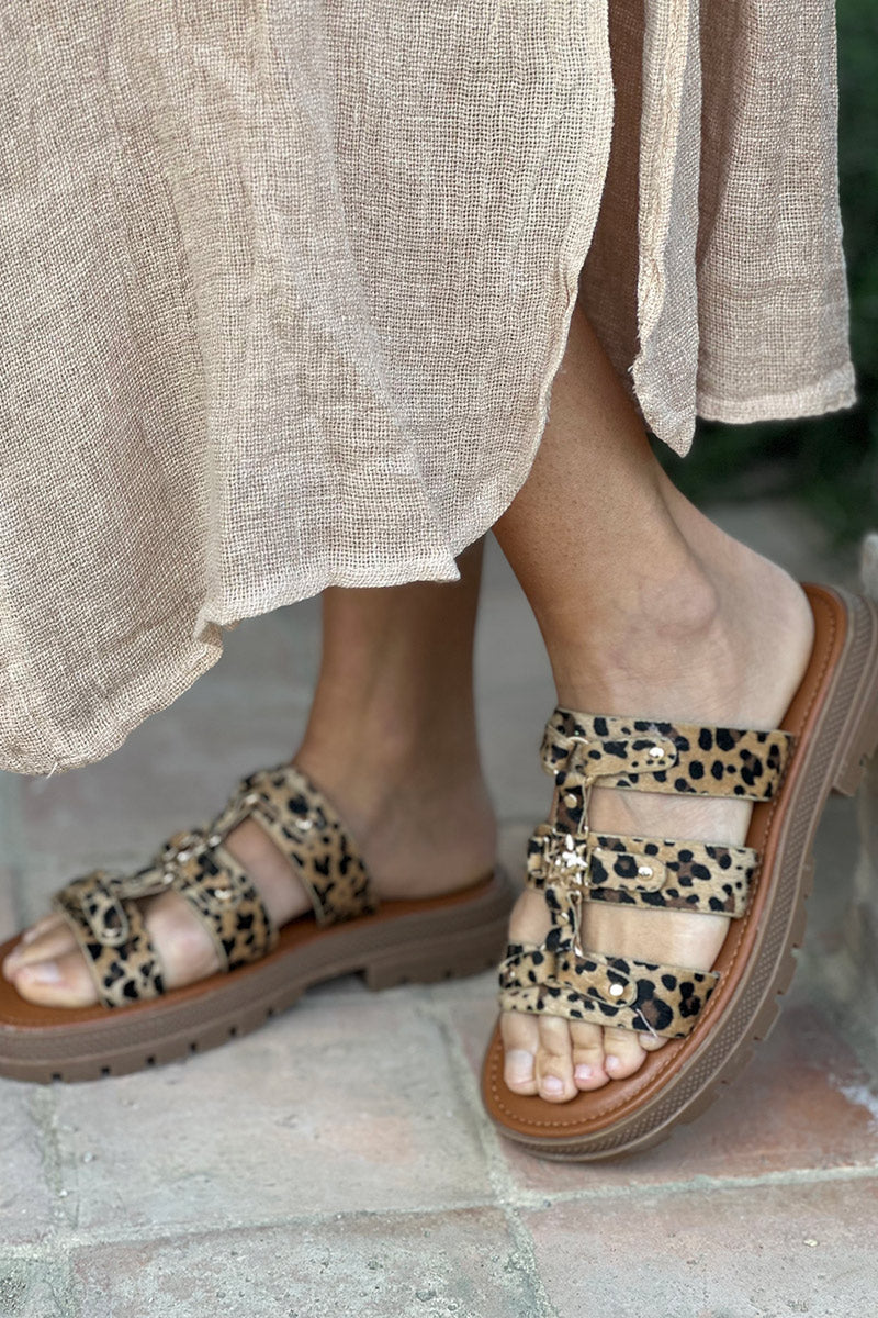 Sandalias planas tipo mules con estampado de leopardo, triple tira dorada y suela con muescas.