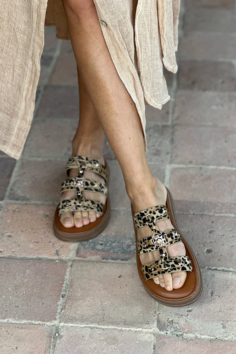 Sandalias planas tipo mules con estampado de leopardo, triple tira dorada y suela con muescas.