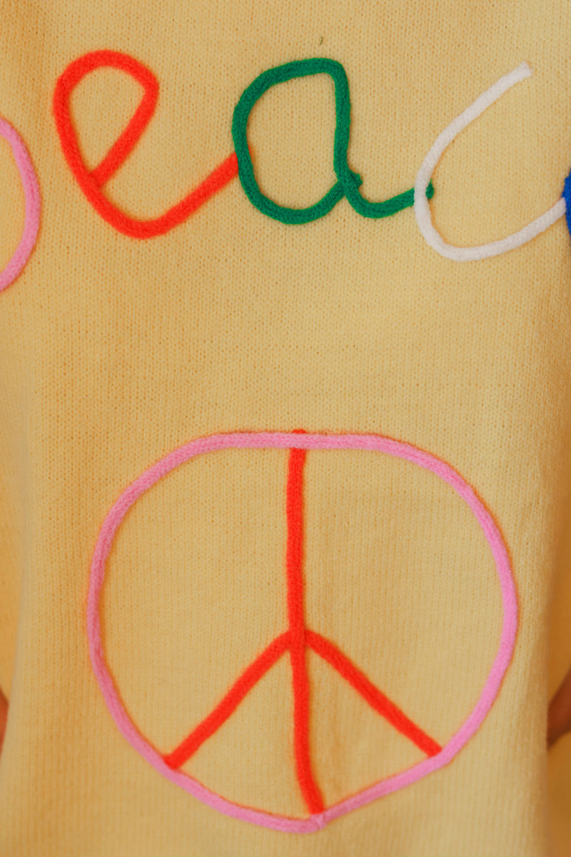 Suéter de manga corta de color amarillo pastel con punto pequeño y suave y bordado de la Paz colorido.