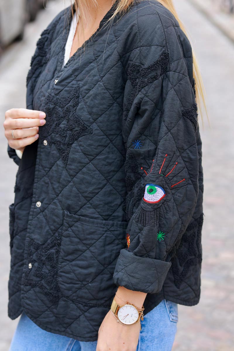 Anorak negro de algodón con botones y bolsillos con bordado de estrellas y ojos.